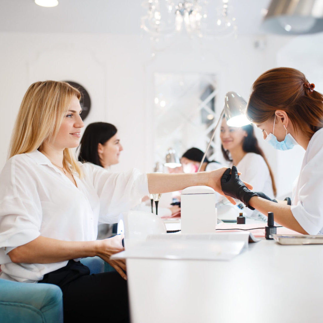 Group of girlfriends relax on manicure procedure in beauty salon. Professional beautician and female customers, nail care in spa, fingernail treatment